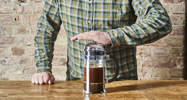 Mann drückt den Stempel von einer French Press nach unten