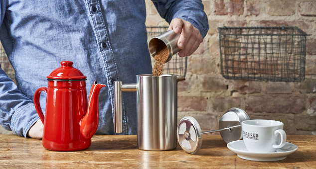 Kaffeepulver wird in Edelstahl French Press gefüllt in rustikalem Ambiente