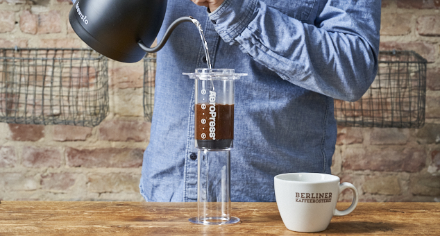 Mann füllt heißes Wasser in eine Aeropress hinein