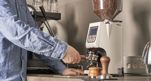 Siebträger wird an einer Kaffeemühle mit Kaffeemehl befüllt