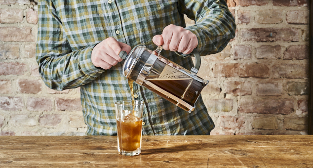 Mann gießt Kaffee mit einer French Press in ein Glas mit Eiswürfeln